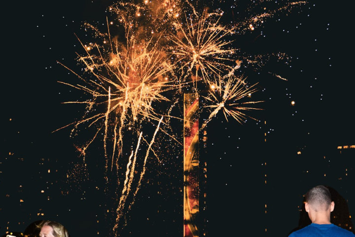People photographing fireworks at night with bright golden bursts in the sky.